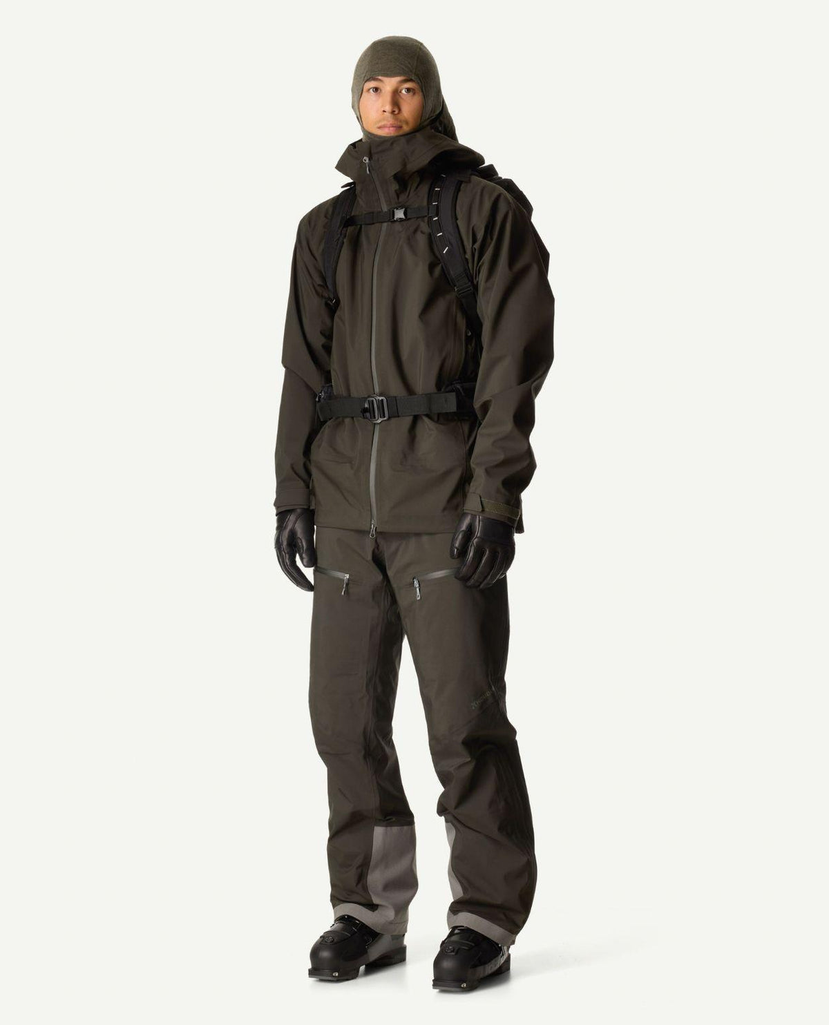 Man i grön skidjacka och matchande byxor, komplett med ryggsäck, mössa och pjäxor.