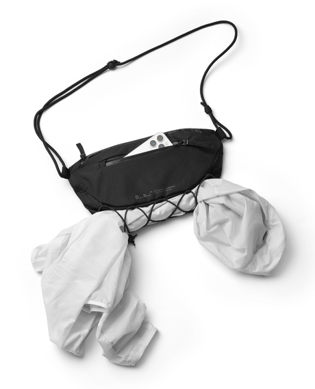 Svart D_b_ Roamer Pro Sling Bag 6L slingväska med mobil i fickan och jacka fastsatt i fronten.