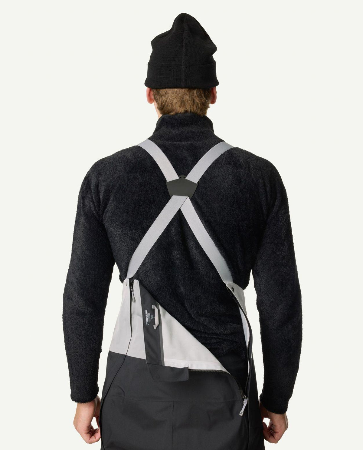 Bakifrånvyn av en person som bär Houdini Rollercoaster Bib Pants II i svart med grå hängslen och en dragkedja öppen i ryggen.