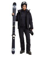 J.Lindeberg Oates Down Jacket Women i svart med skidor, skidglasögon och pjäxor.