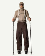 Skidåkare i brunt Houdini Rollercoaster Bib Pants-ställ med skidstavar.