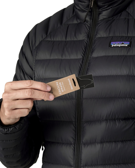 Närbild på person som håller i lagningslappar framför svarta dunjackan Patagonia Down Sweater Women