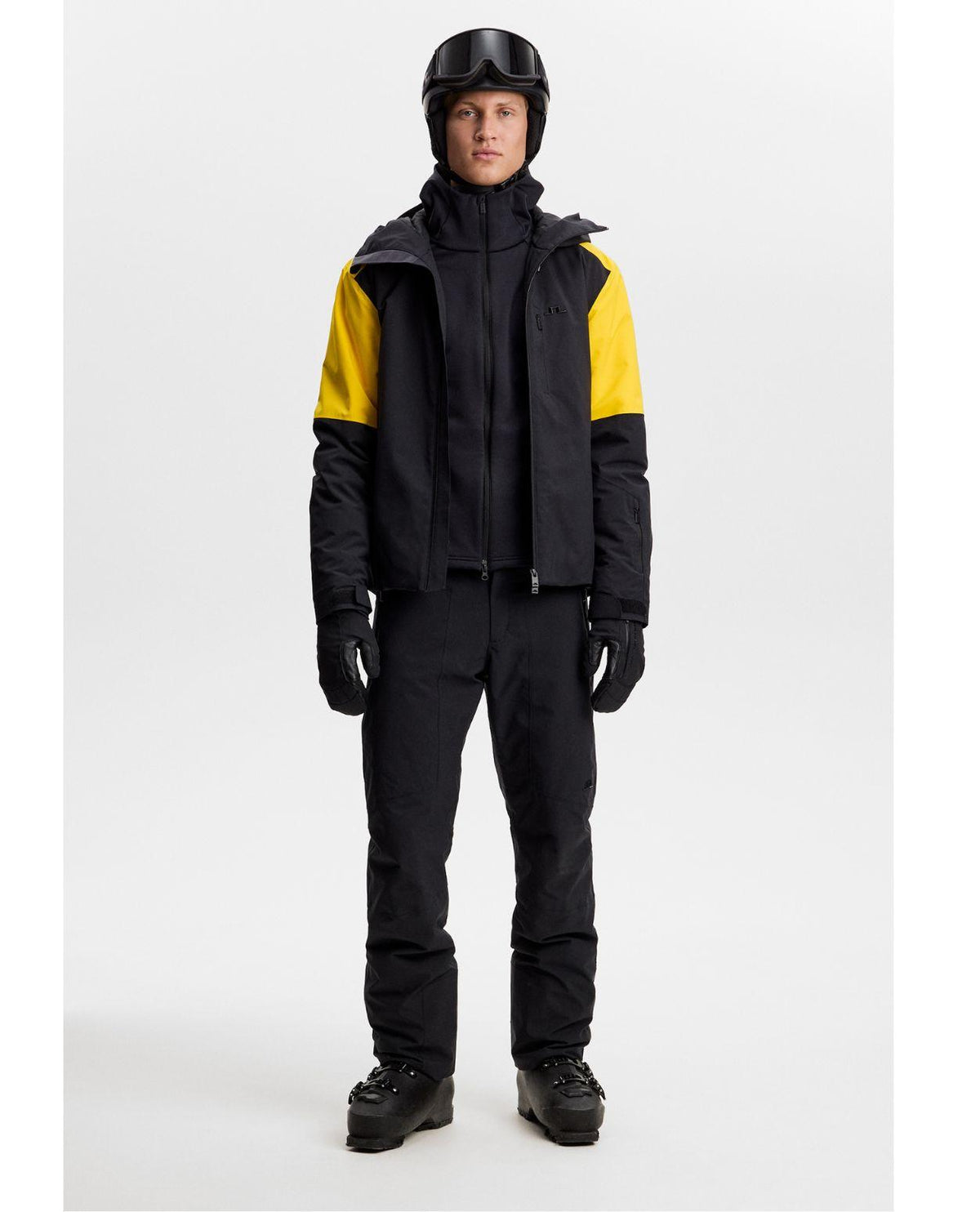 Skidåkare i J.Lindeberg Pollock Polartec Hood mellanlager med svart och gul skidjacka samt matchande byxor.