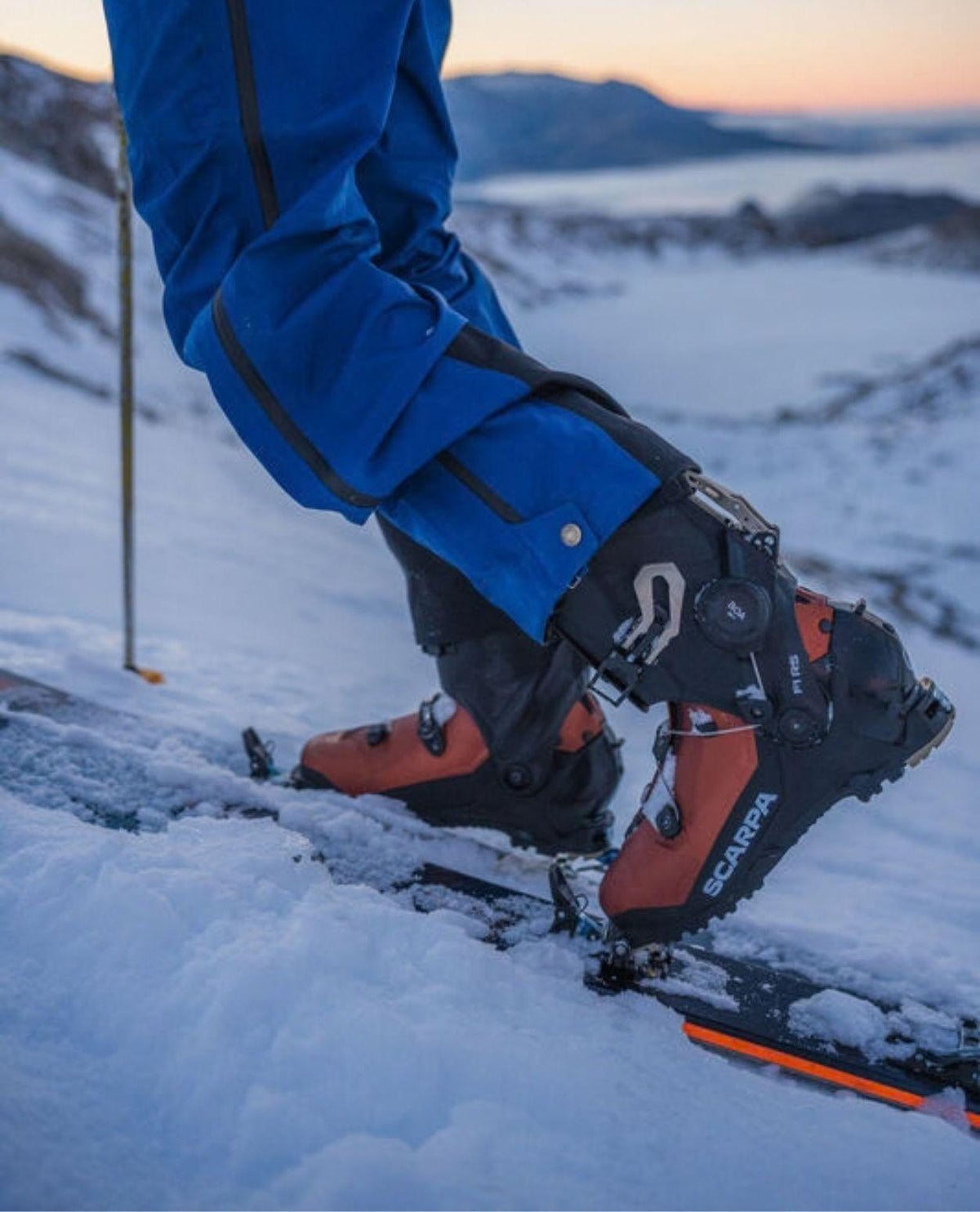 Scarpa F1 RS toppturspjäxor i brun och svart färg vid skidåkning i snöigt fjällandskap.