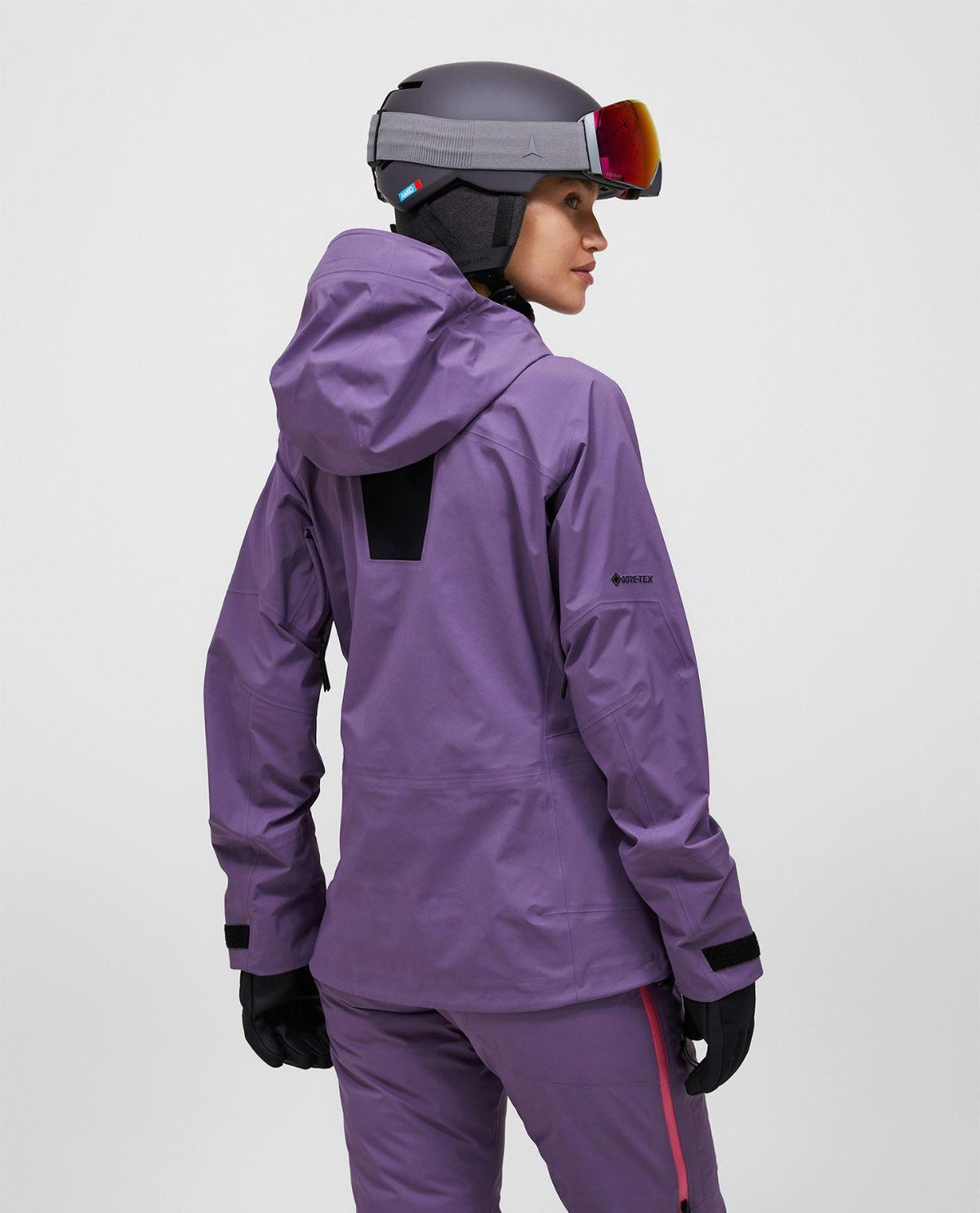 Peak Performance Alpine Gore-Tex 3L Jacket Women i lila färg, visad bakifrån på skidåkare med hjälm och skidglasögon.